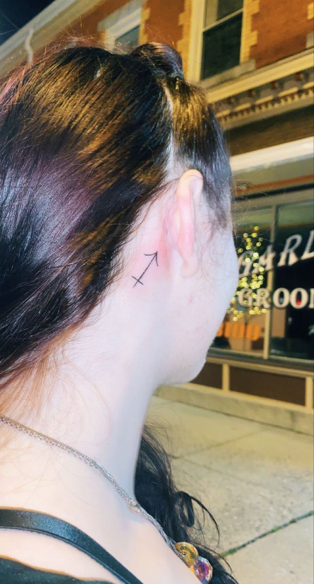 the back of a woman's head with a small cross tattoo on her left ear