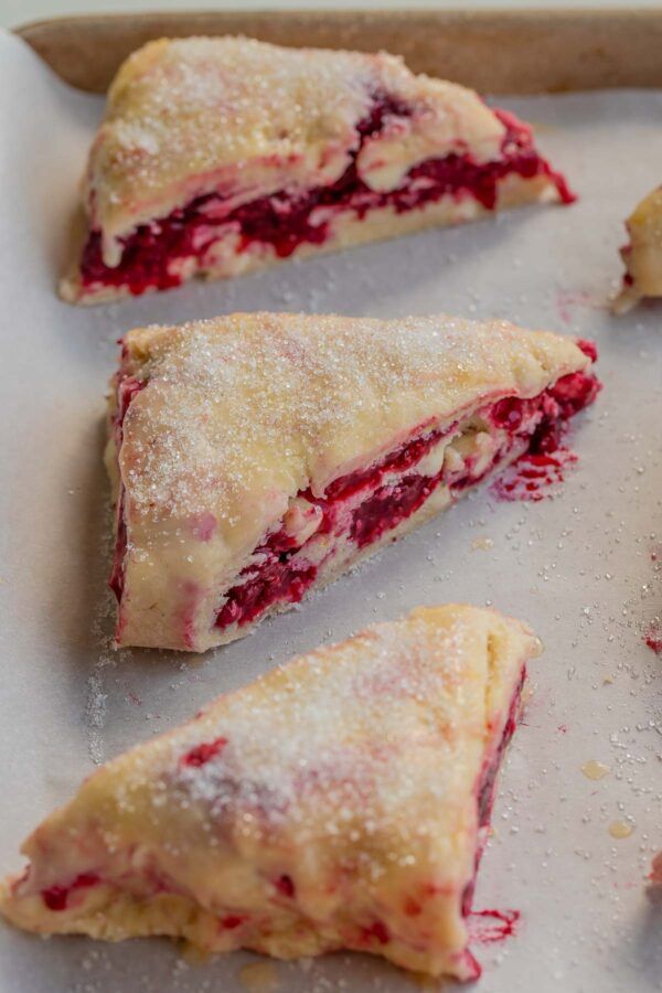 four pastries on a baking sheet with powdered sugar and cranberry sauce