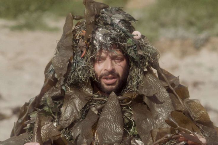 a man wearing a bird nest on top of his head while holding something in his hands