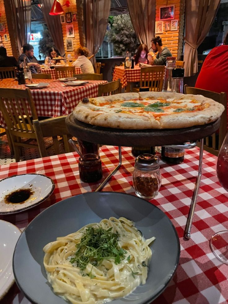 two pizzas and pasta on a table with red checkered tablecloth in a restaurant