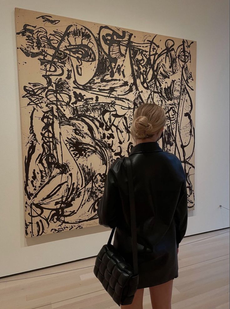 a woman standing in front of a large painting on display at an art gallery with her back to the camera