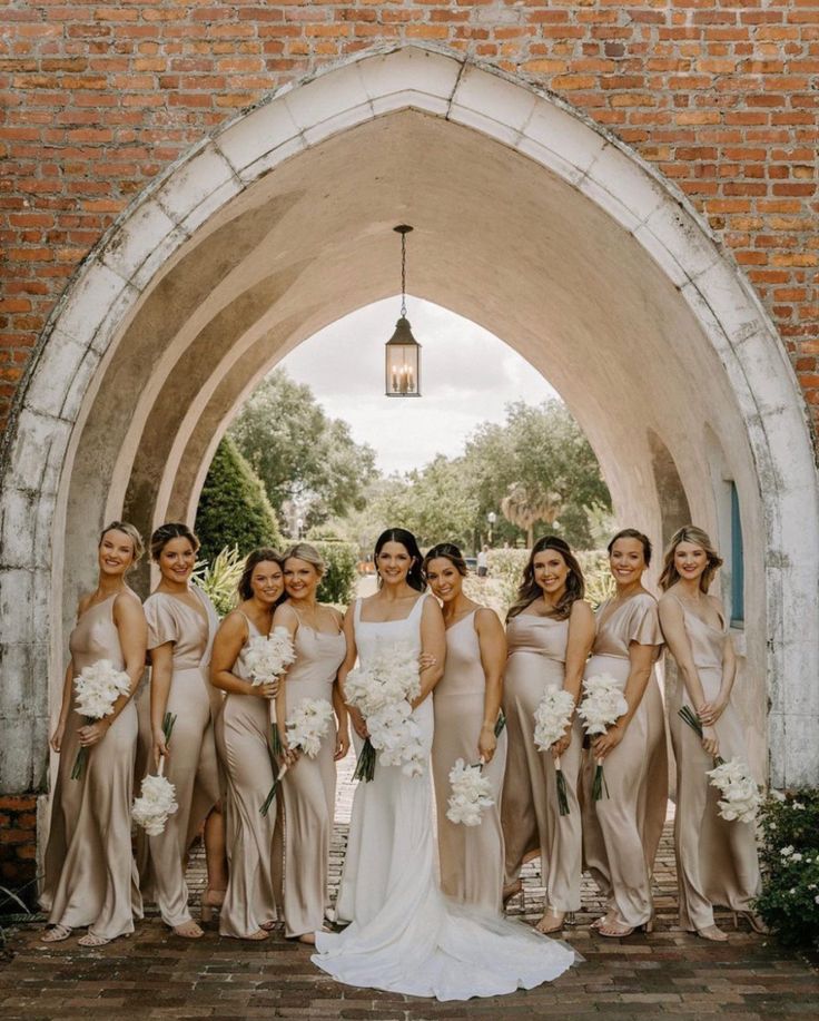 a group of women standing next to each other in front of a brick wall holding bouquets