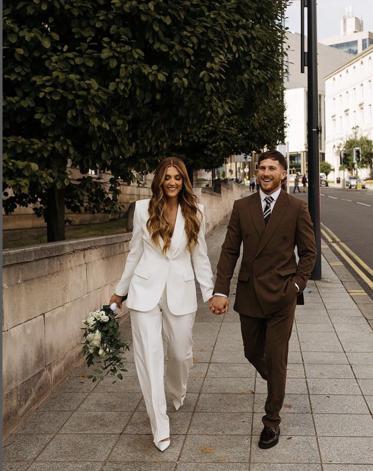 a man and woman are walking down the street holding hands while dressed in white suits