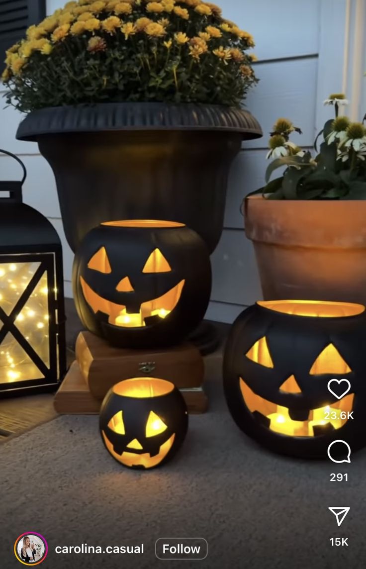 three pumpkins are lit up in front of a potted plant and two lanterns