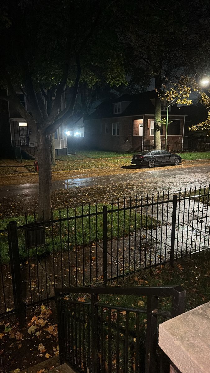 an old car is parked on the street in front of a fenced area at night