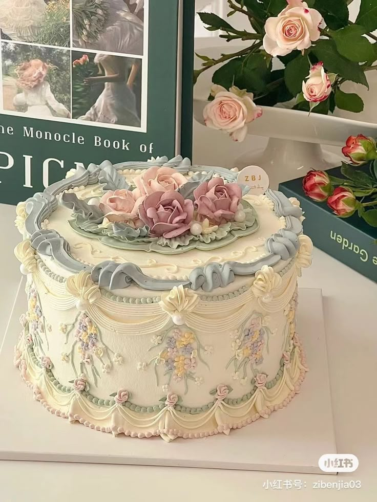 there is a cake on the table with flowers around it and a book in the background