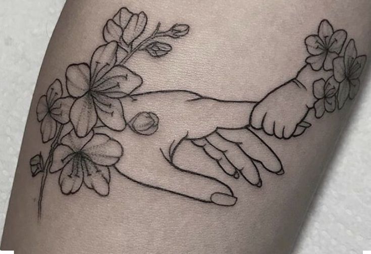 two hands holding each other with flowers on their arm and behind them is the outline of a woman's hand