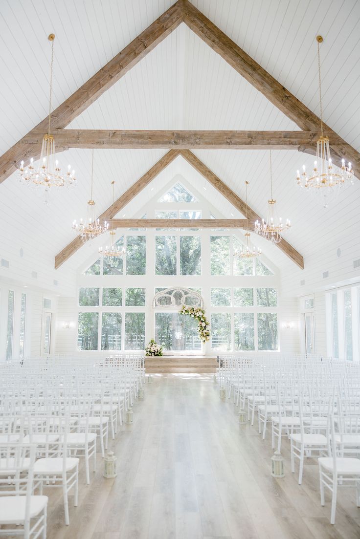 an indoor wedding venue with white chairs and chandelier hanging from the ceiling in front of large windows