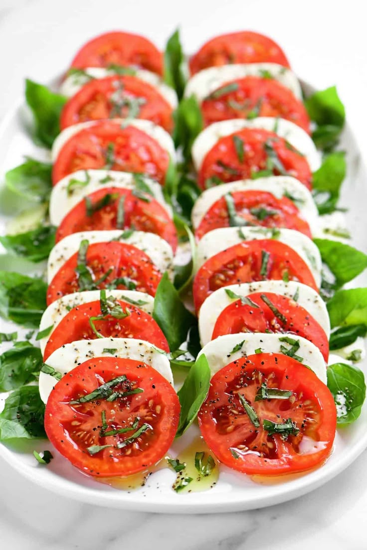 tomato and mozzarella appetizer on a white platter with fresh basil