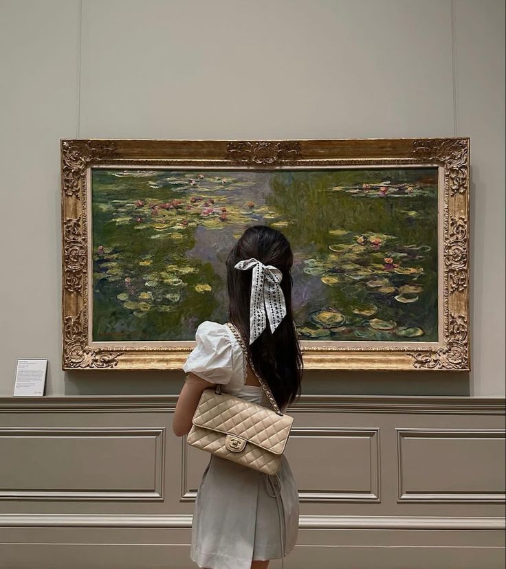 a woman standing in front of a painting holding a basket and looking at the water lily pond