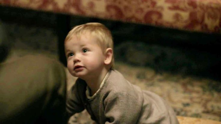 a little boy sitting on the floor looking up at something in front of his face