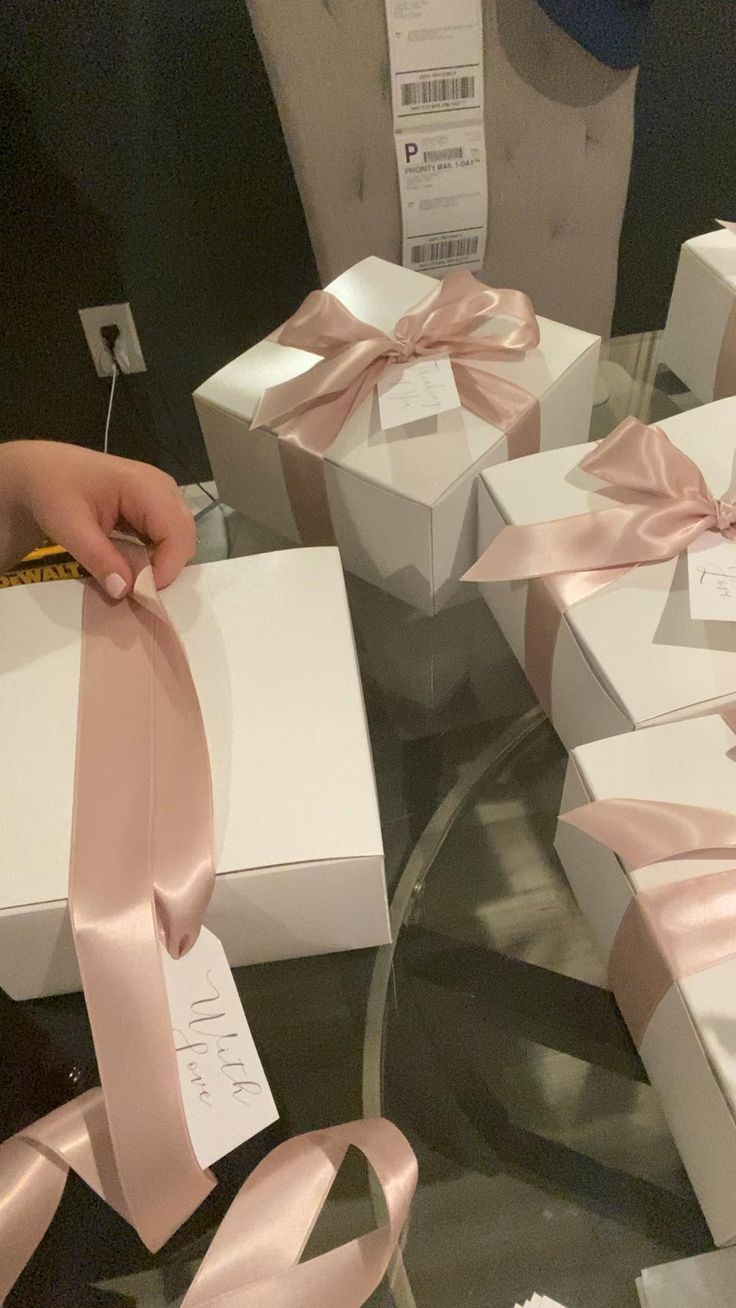 several white boxes with pink ribbons and tags on them are sitting on a glass table