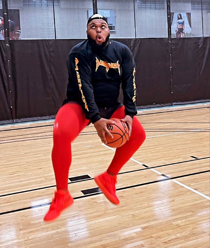 a man in red leggings holding a basketball on top of a wooden floor