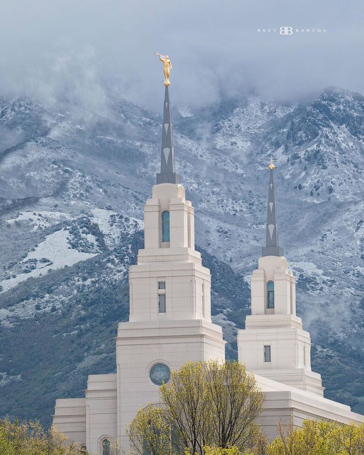 a large white building with two towers and a gold statue on top in front of snow covered mountains