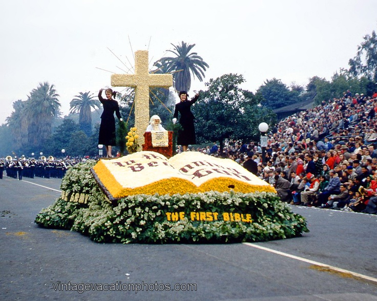 two people standing on top of a large cross in the middle of a street with other people watching