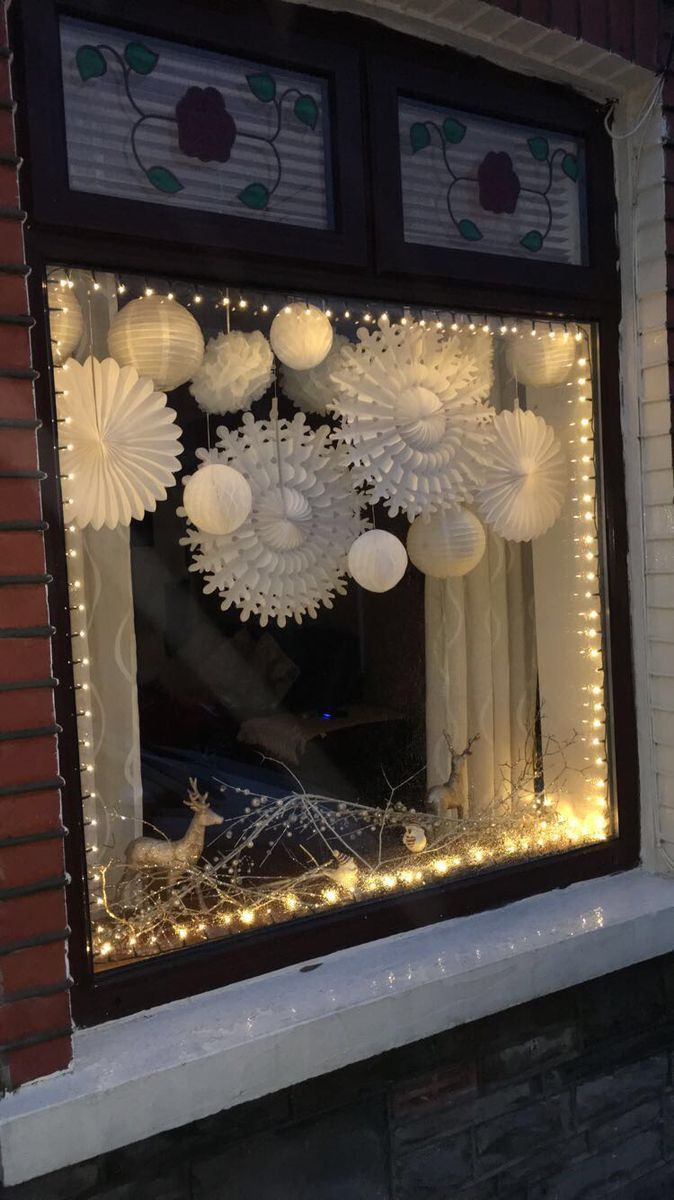 a window decorated with white paper fans and christmas lights in front of a brick building