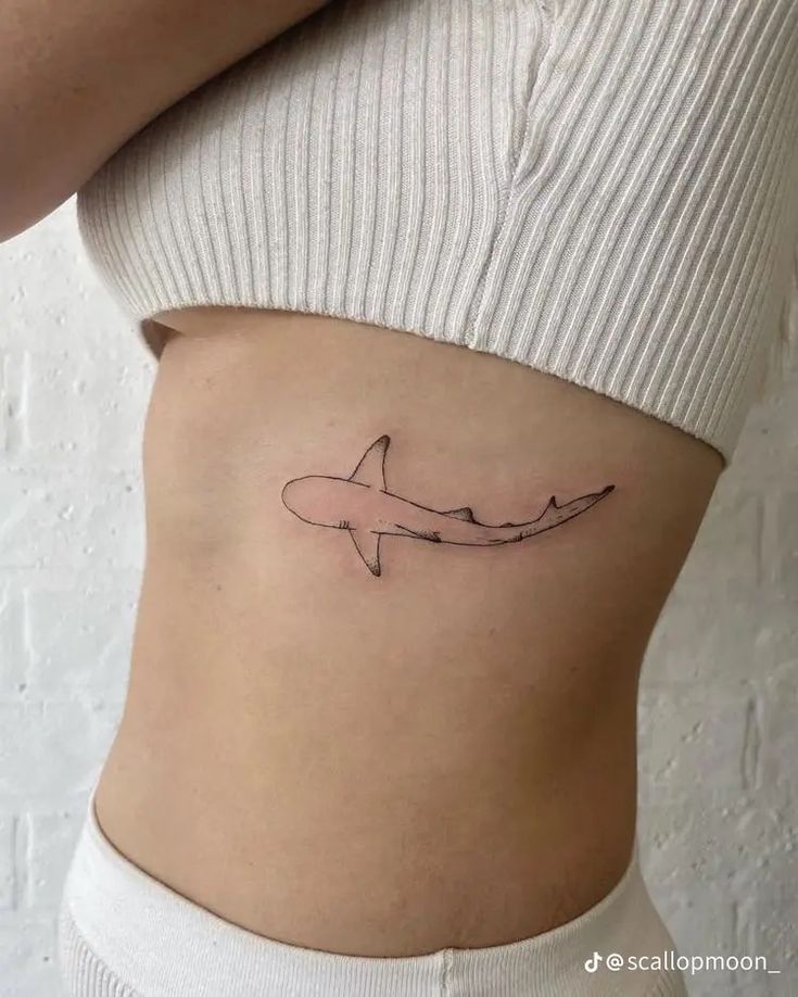 a woman's stomach with a small tattoo of a shark on the side of her belly