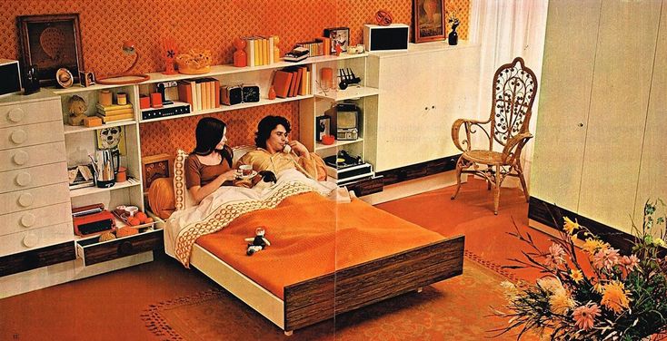 two women sitting on an orange bed in a room with bookshelves and shelves