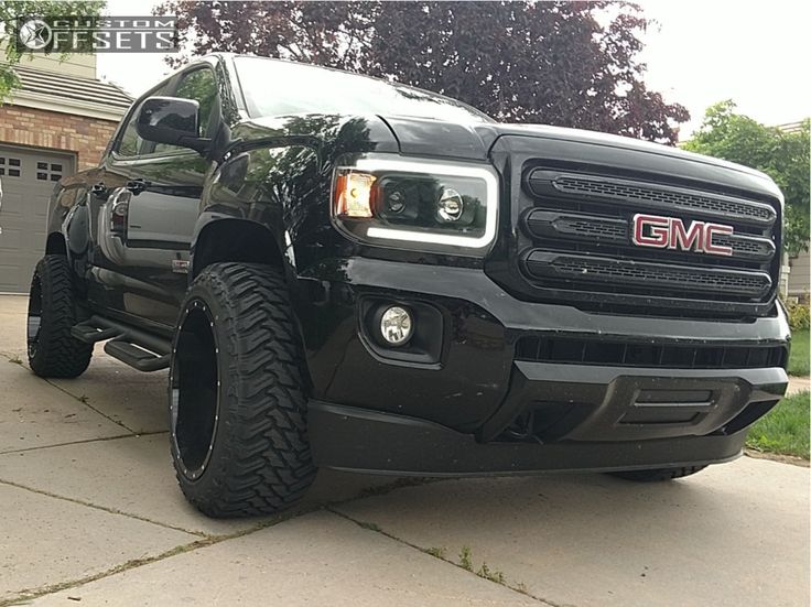 a black truck is parked in front of a garage with its lights on and it's hood up