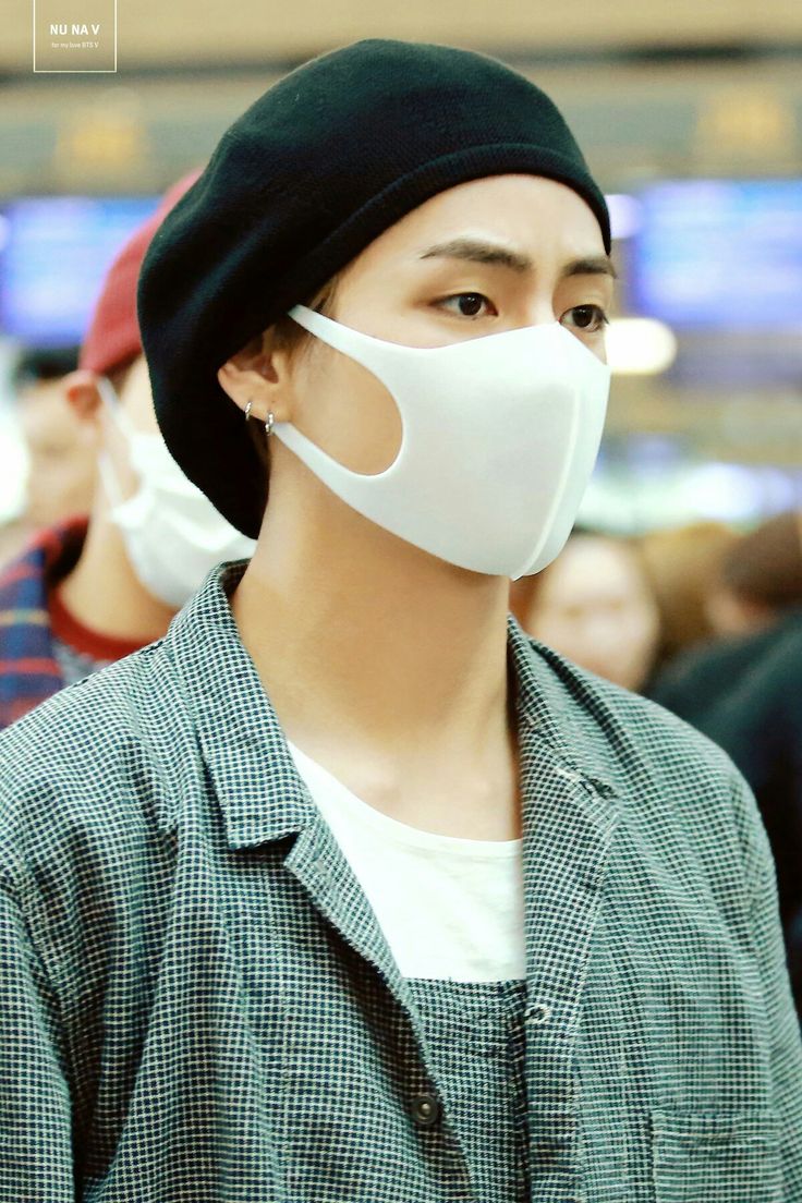 a man wearing a white face mask in front of a group of people at an airport