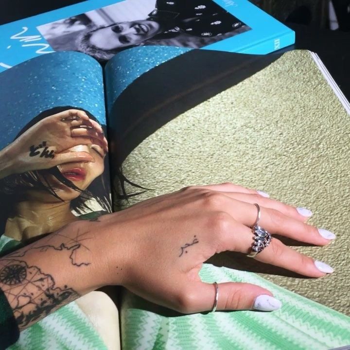 a woman's hand on top of an open book with her face and hands tattooed