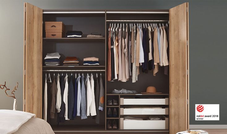 an open closet with clothes and boxes on the floor next to a bed in a bedroom