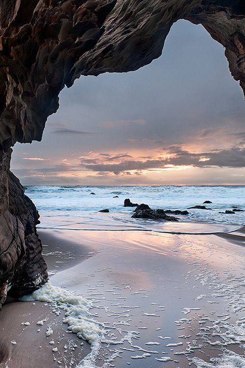 a black and white photo of a beach with waves coming in from the ocean under an arch