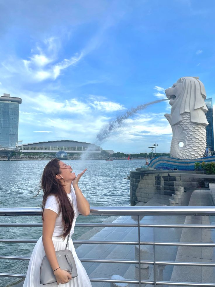 a woman standing on the side of a bridge next to a body of water with a statue in the background