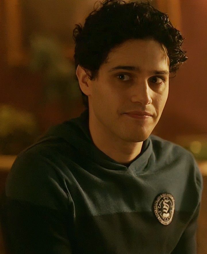 a young man with curly hair wearing a green shirt and looking at the camera while sitting down