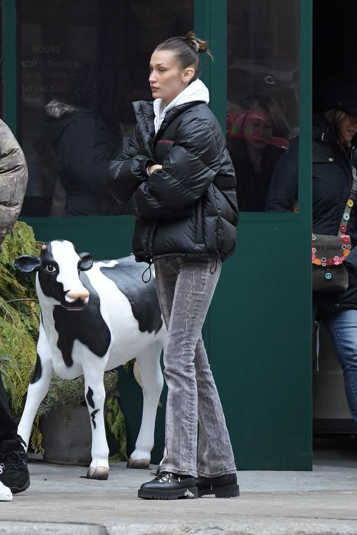 a woman standing next to a black and white cow in front of a green building