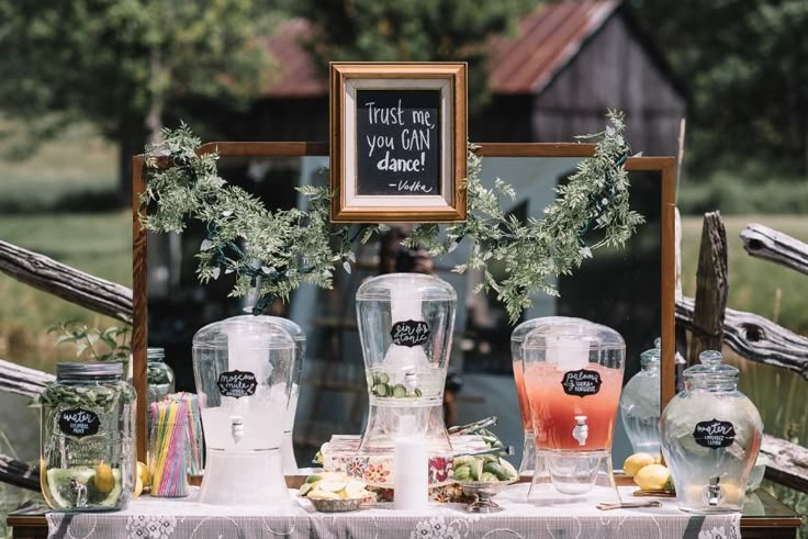 a table topped with lots of bottles and glasses filled with liquid next to a framed sign