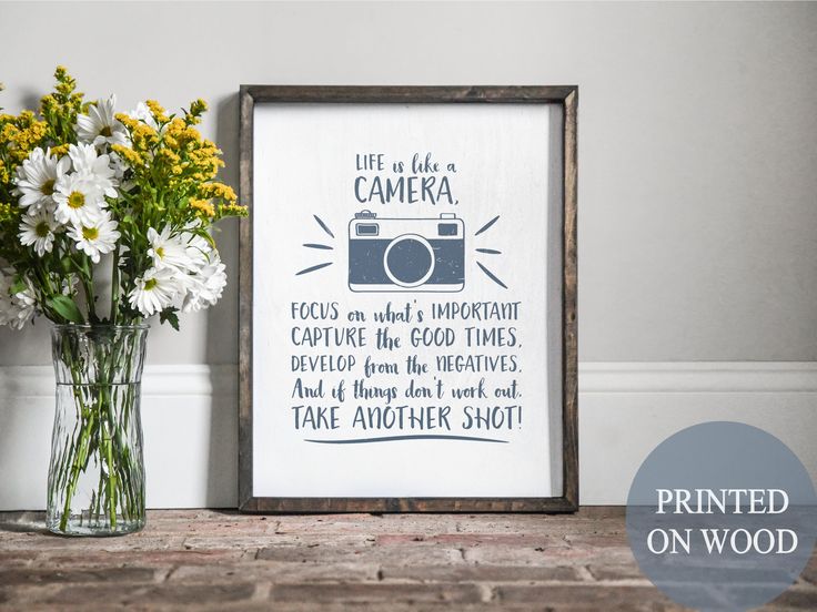 a vase with flowers and a framed photograph on a table next to a wooden frame