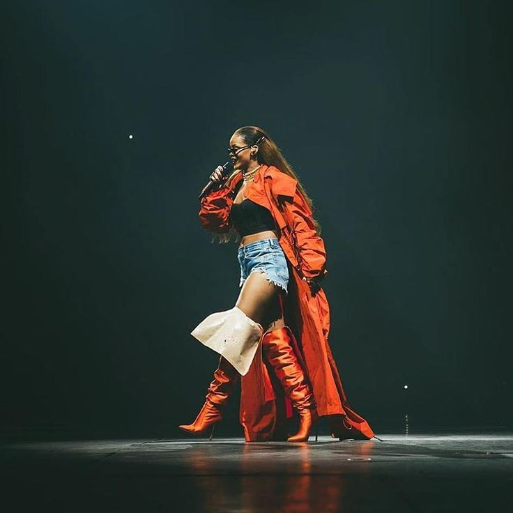 a woman in an orange coat and blue shorts on stage with her legs spread out