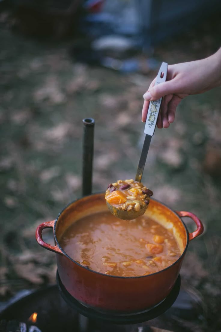 a person holding a knife over a pot filled with food