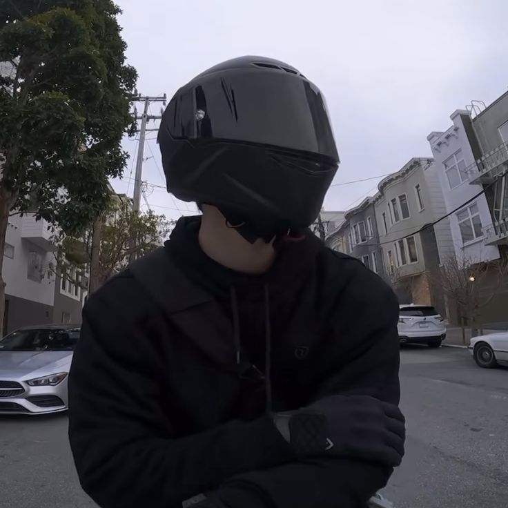 a man wearing a black jacket and helmet riding a skateboard down a street next to parked cars