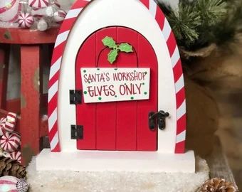 a red and white christmas decoration with a santa's workshop sign on the door