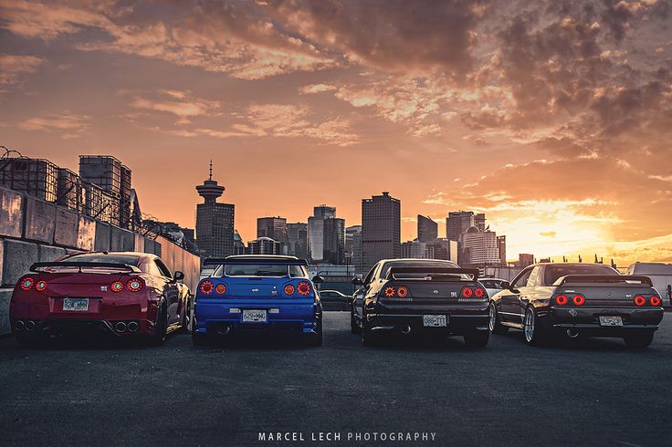 four cars are parked in front of a cityscape with the sun setting behind them