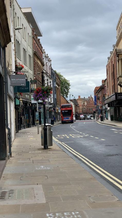 a red double decker bus driving down a street next to tall buildings on either side