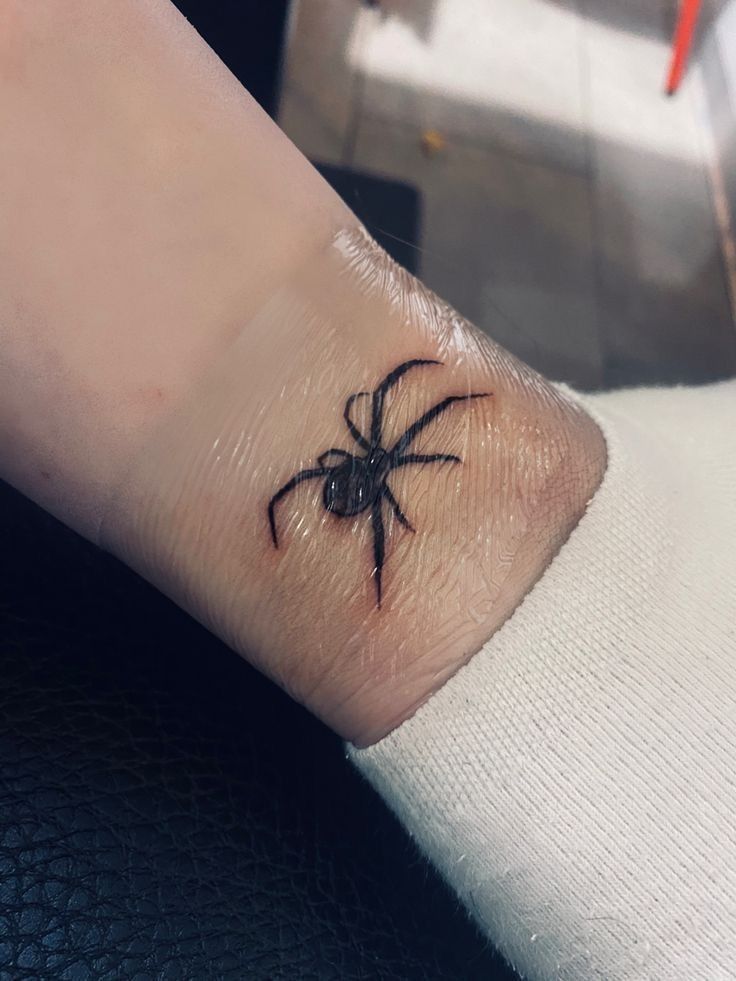 a small black spider tattoo on the wrist