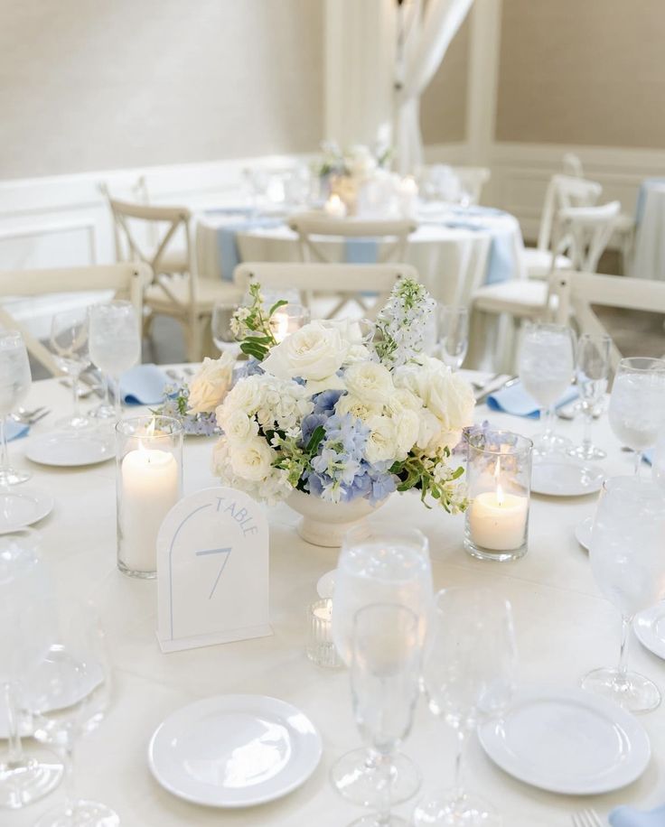 a white table topped with lots of plates and glasses filled with flowers next to candles