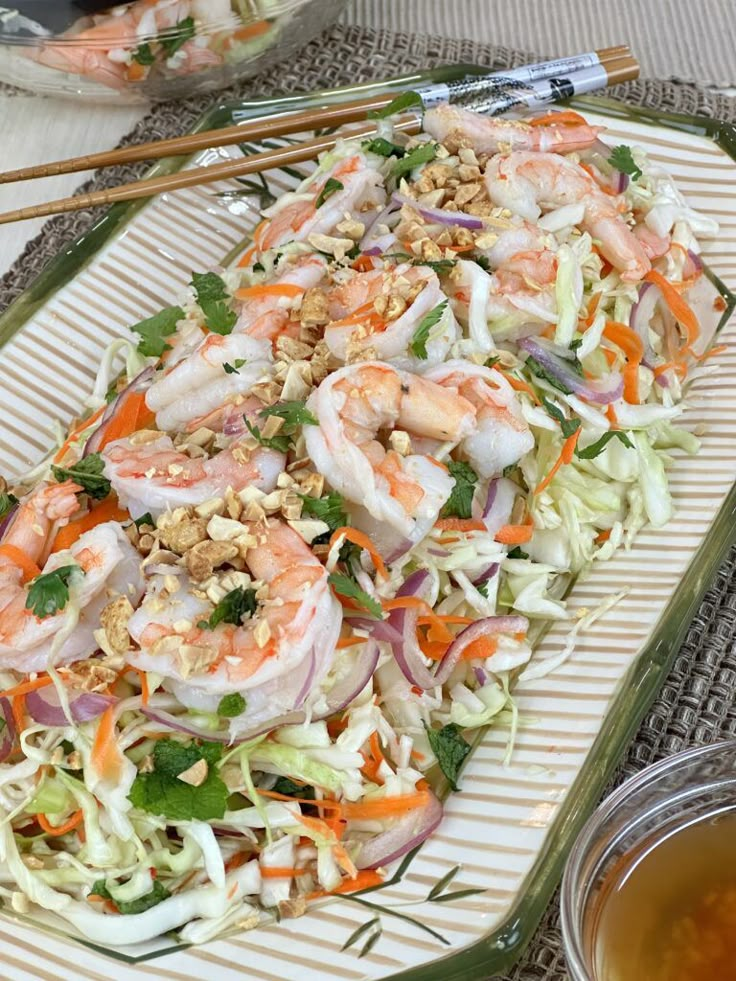 shrimp salad with carrots, lettuce and nuts on a plate next to chopsticks