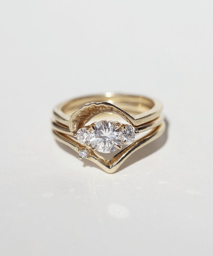 three gold rings with two diamonds on each ring and one diamond in the middle, sitting on a white surface