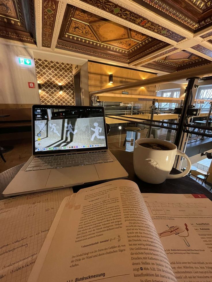 an open book sitting on top of a table next to a laptop computer and cup of coffee