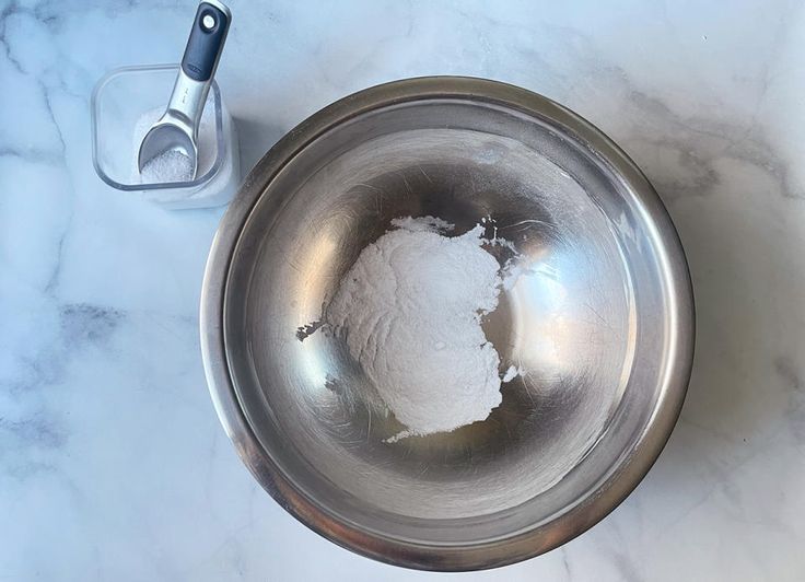 a metal bowl filled with white powder next to a measuring spoon on a marble counter top