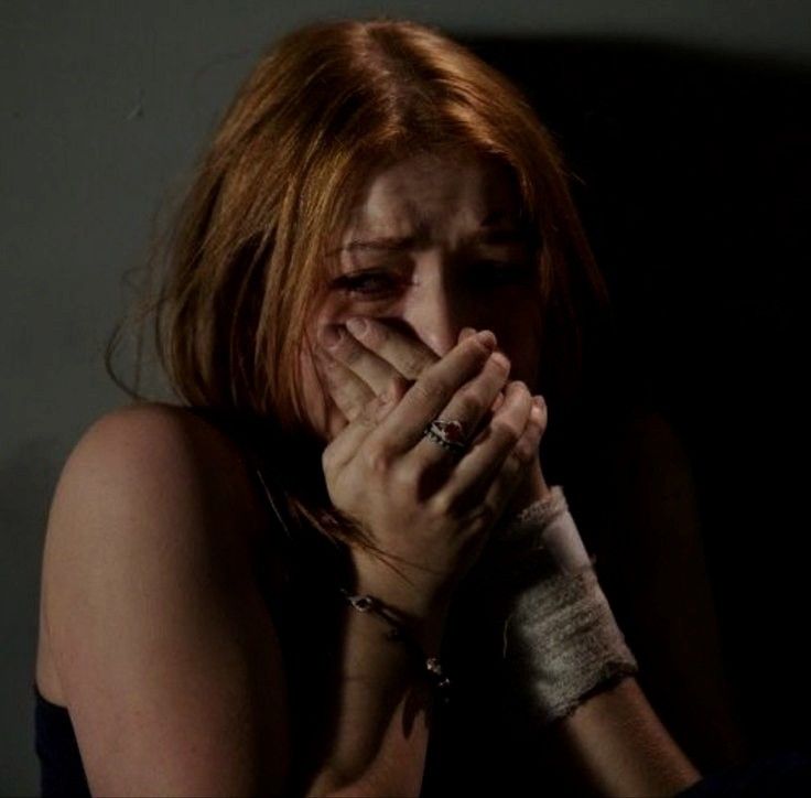 a woman with bandages covering her face and hand in front of her face, sitting on a bed