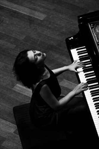 a woman sitting at a piano with her hands on the keys and looking up into the sky