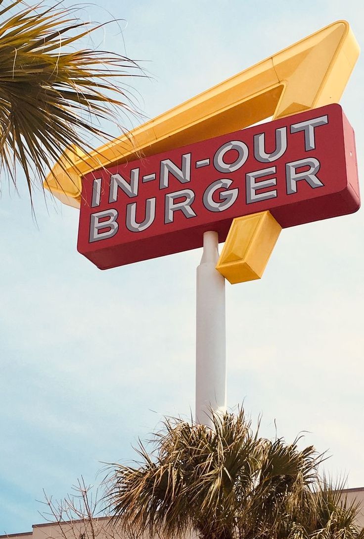 a close up of a restaurant sign with palm trees in the foreground and a building in the background