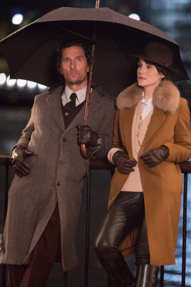 a man and woman standing under an umbrella in the rain, dressed in leathers