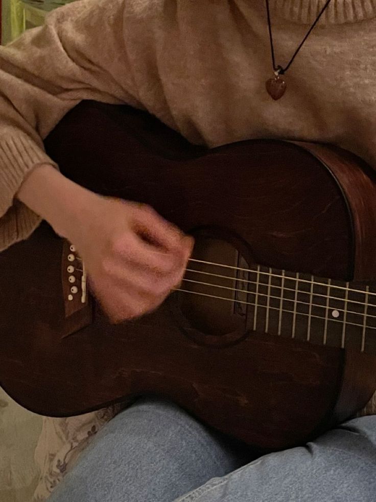 a person sitting on a couch playing an acoustic guitar with one hand and the other