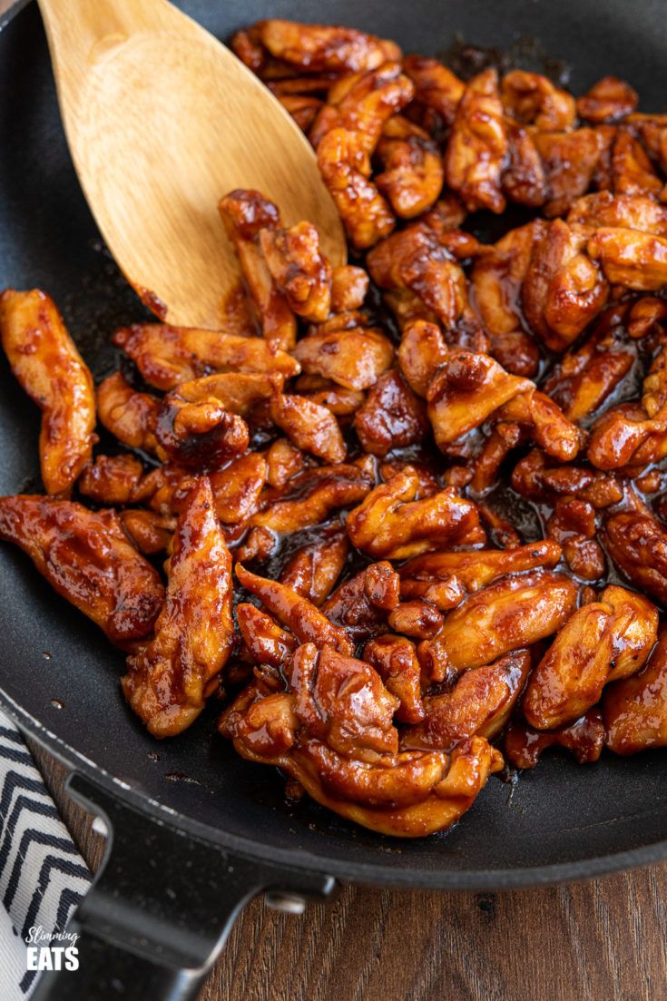 chicken wings being cooked in a skillet with a wooden spoon